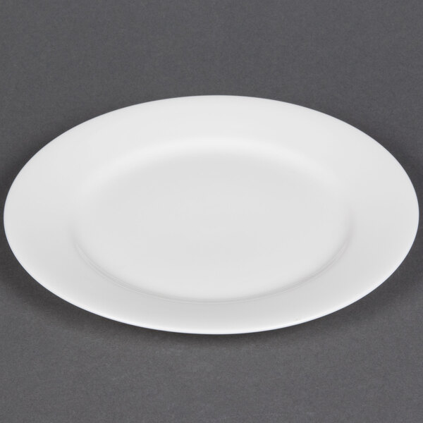 A CAC white bone china plate with a small rim on a gray surface.