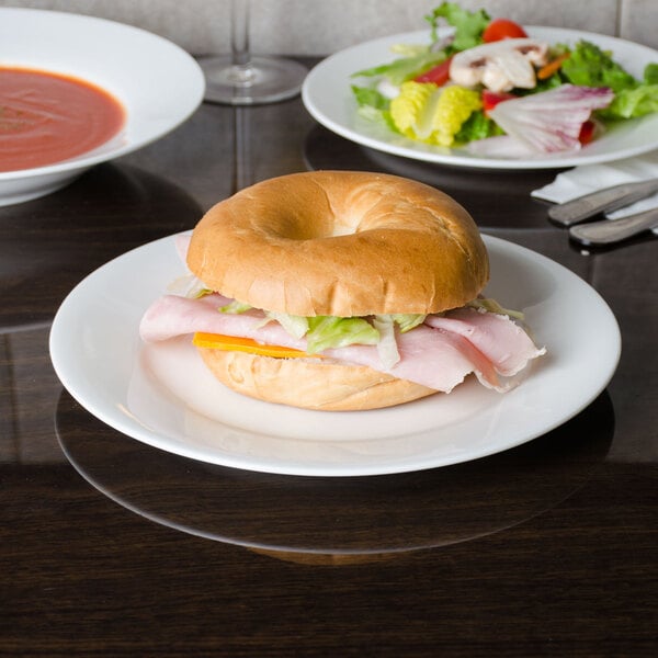 A CAC Majesty European bone china plate with a bagel sandwich, salad, and silverware.