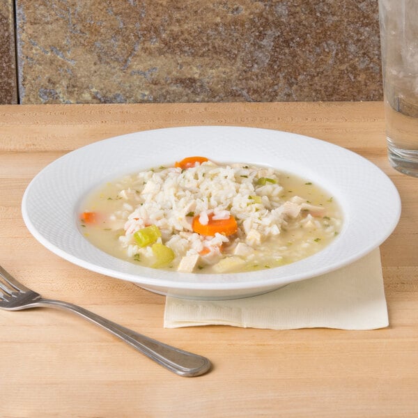 A CAC Boston white porcelain soup bowl filled with soup, rice, and vegetables with a spoon.