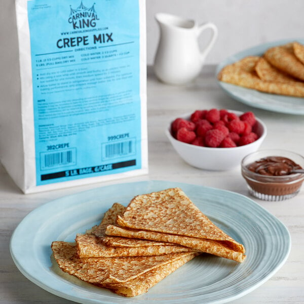 Crepe mix sits beside three cooked and folded plain crepes, a bowl of raspberries, and a bowl of Nut