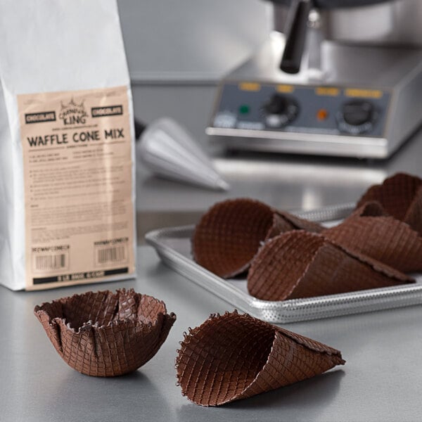 A brown waffle cone with white chocolate on a tray next to Carnival King Chocolate Waffle Cone Mix.