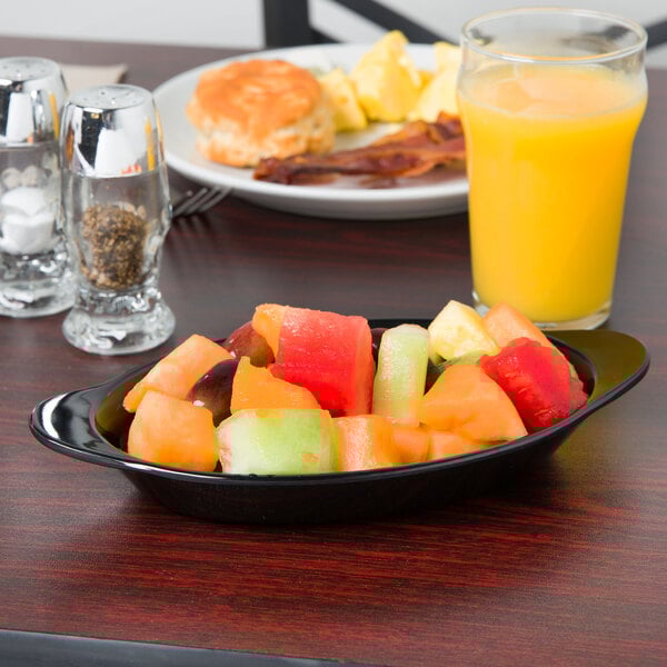 A black oval side dish with fruit on a table.
