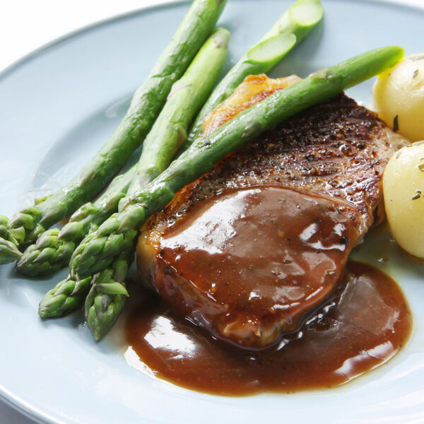 A plate of food with beef, potatoes, and asparagus topped with Chef's Companion Beef Gravy.