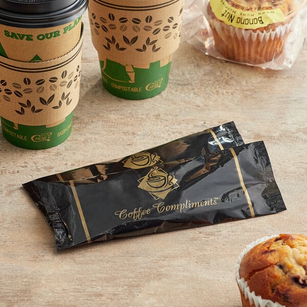 A black and gold Single Serving Hot Beverage Condiment Kit packet next to a couple of coffee cups on a counter.