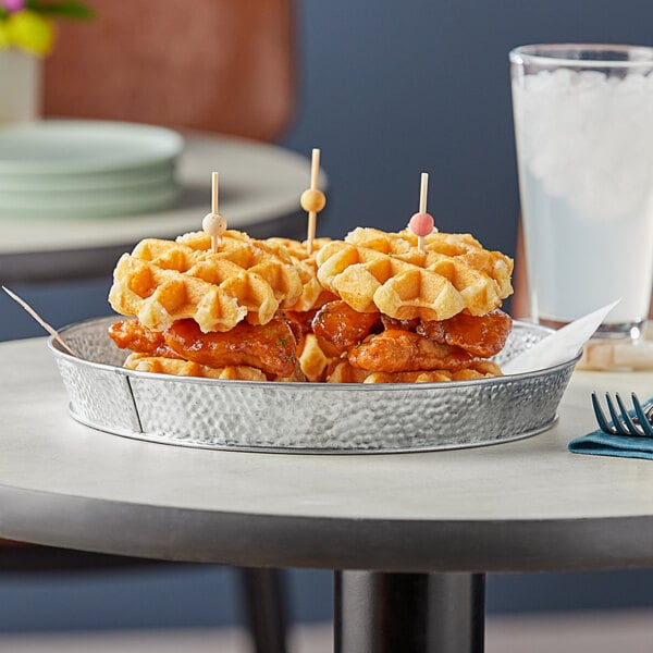 A Tablecraft galvanized steel platter holding a plate of waffles with chicken and a fork.