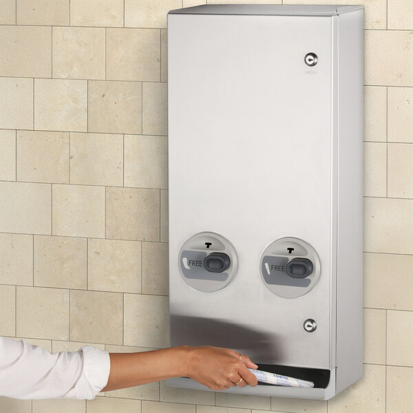 A white machine with a person's arm using a Bobrick sanitary napkin/tampon dispenser.