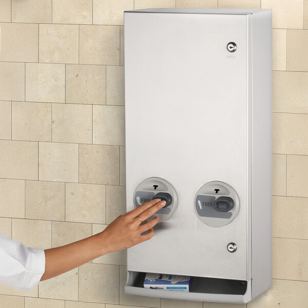 A hand pressing a button on a white box with "Bobrick" on it.