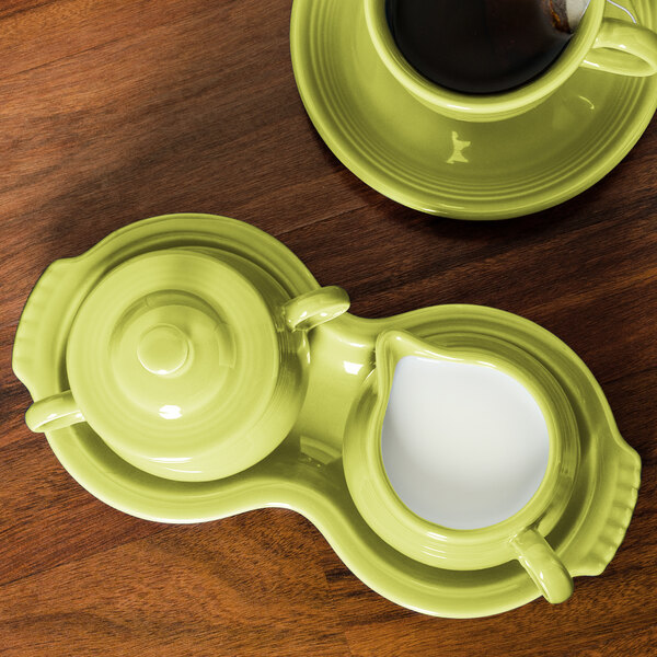 A green Fiesta sugar and creamer tray with a brown liquid in the creamer and a cup of coffee on top.