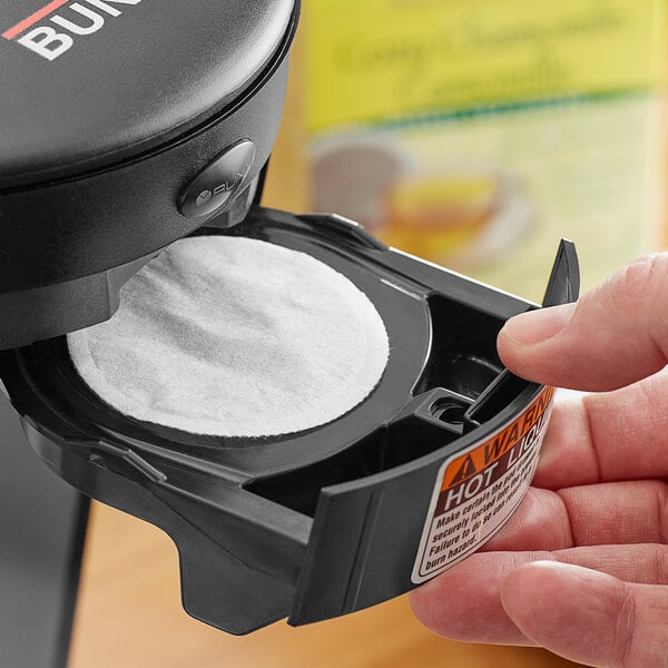 A hand placing a Bigelow Cozy Chamomile Herbal Tea single serve pod into a coffee maker.