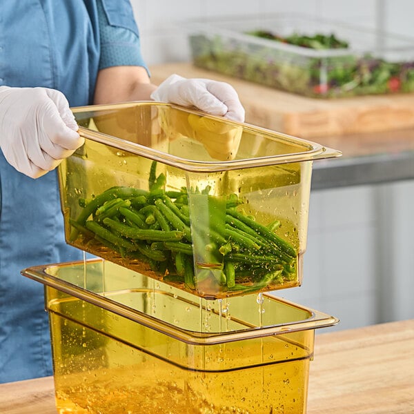 A person in a blue uniform using a Cambro amber plastic colander pan to drain green beans.