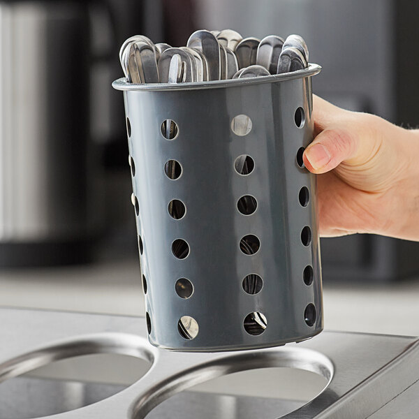 A hand holding a Steril-Sil gray plastic flatware cylinder full of spoons.