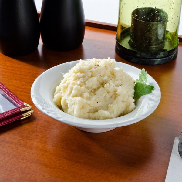 A Tuxton bright white china bowl filled with mashed potatoes on a table.