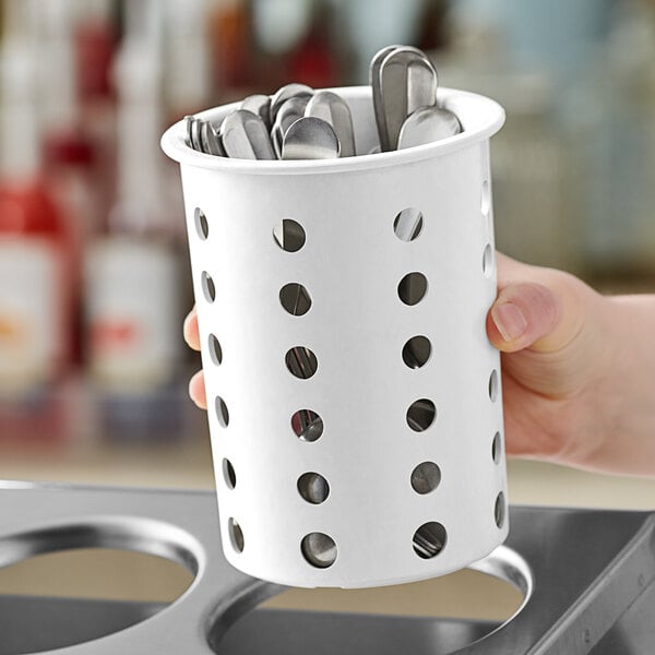 A hand holding a white Steril-Sil flatware cylinder with metal utensils inside.