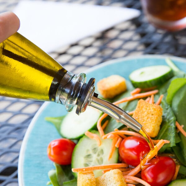 A person using a Tablecraft recycled green glass oil and vinegar dispenser to pour oil into a salad.