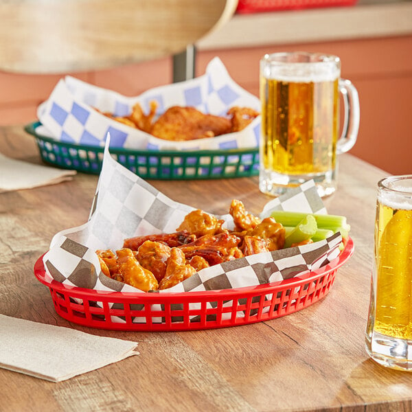 A red Tablecraft oval polypropylene basket filled with chicken wings and celery on a table.