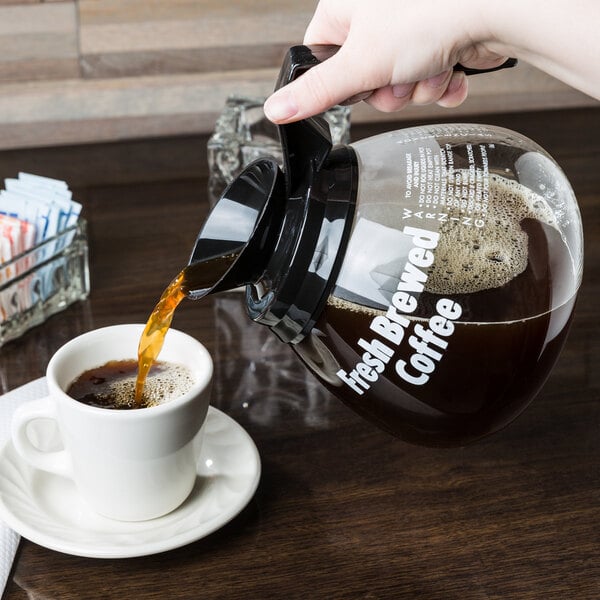 A person pouring coffee from a Grindmaster coffee decanter into a cup.