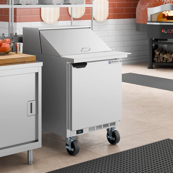 A stainless steel refrigerated sandwich prep table with a single door and a mega top design, equipped with casters for mobility.