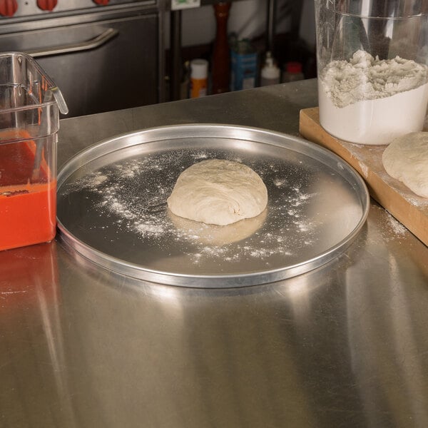 A dough ball on an American Metalcraft aluminum pizza pan on a counter.