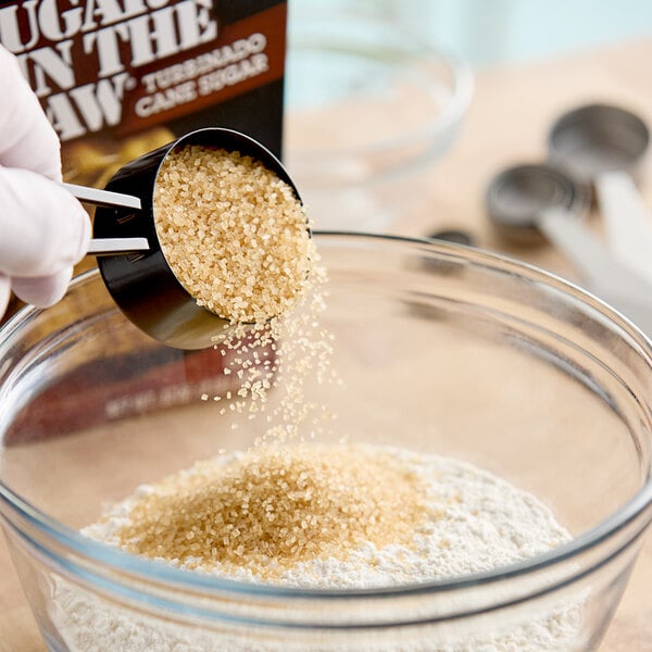 A person using a spoon to pour Sugar In The Raw into a bowl.