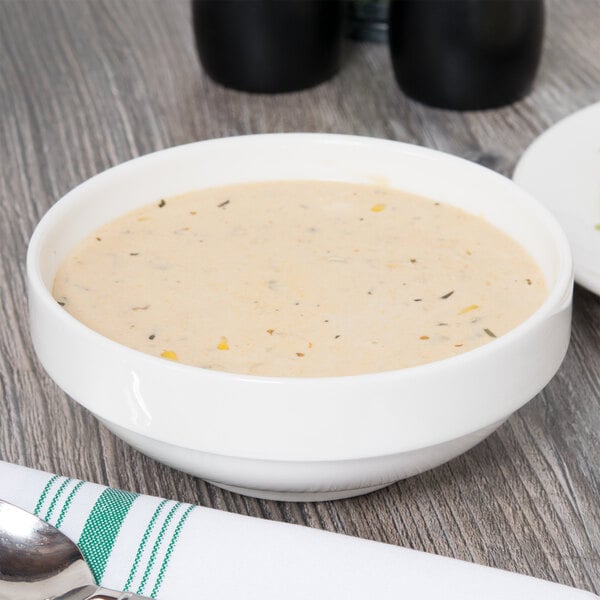 A close up of a Homer Laughlin bright white bowl filled with soup on a wooden table.