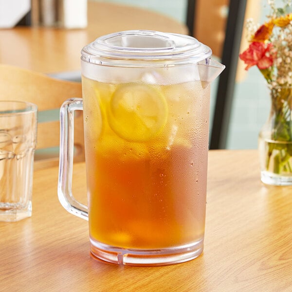 A clear glass pitcher of iced tea with lemon slices on a table.