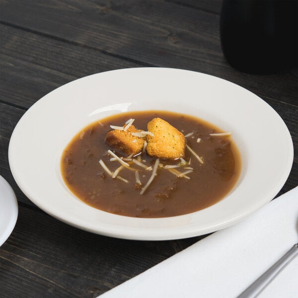 A Homer Laughlin ivory china soup bowl filled with soup and croutons on a table.