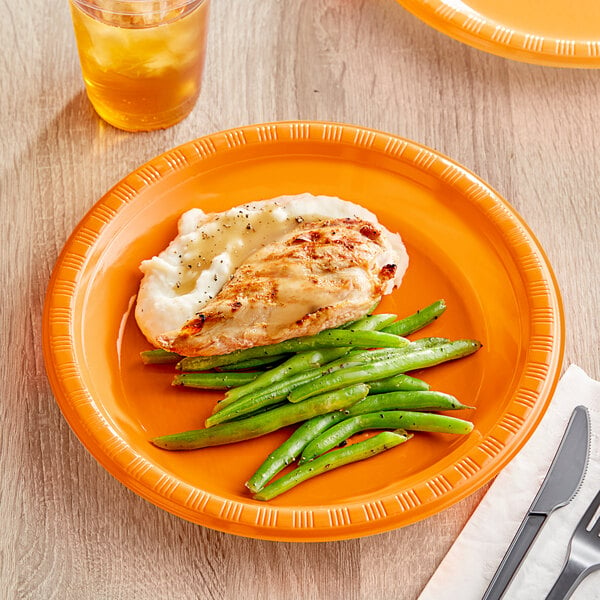 A Sunkissed Orange plastic plate with chicken and green beans on it.