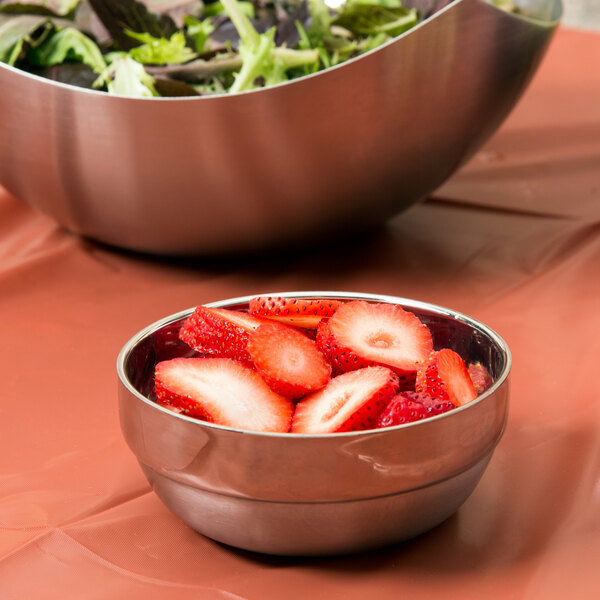 A bowl of strawberries next to a bowl of salad in American Metalcraft stainless steel bowls.