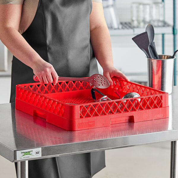 A woman in an apron holding a red Vollrath Traex flatware rack with red and silver utensils inside.