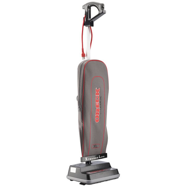 An Oreck upright bagged vacuum cleaner with a grey bag and red and white text on the vacuum.