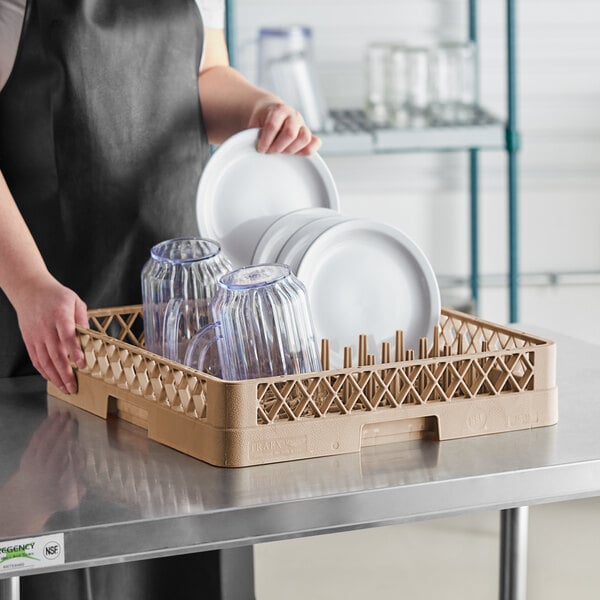 A woman holding a Vollrath TR15 beige dish rack full of plates.