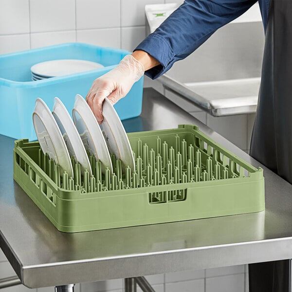 A person putting plates in a Vollrath light green dish rack.