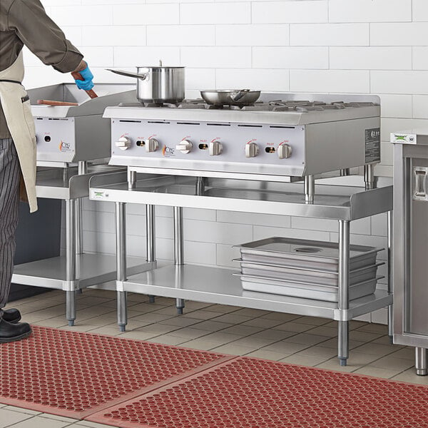 A man in a white apron standing on a Regency stainless steel equipment stand in a professional kitchen.