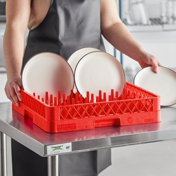 A woman using a Vollrath red plate rack to hold white plates.