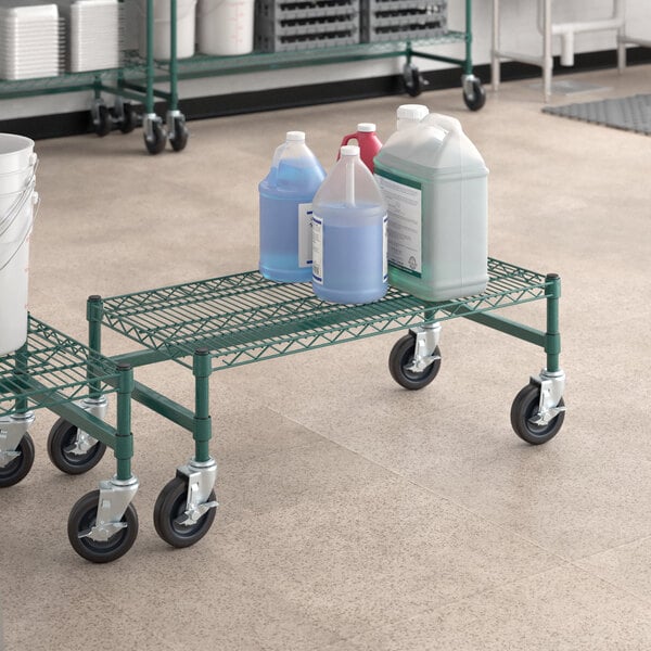 A Regency green epoxy coated mobile dunnage rack with bottles of liquid on it.