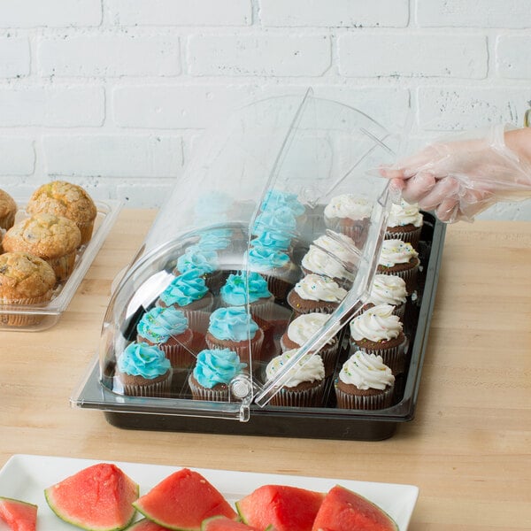 A person holding a black polycarbonate tray of cupcakes with frosting in it.