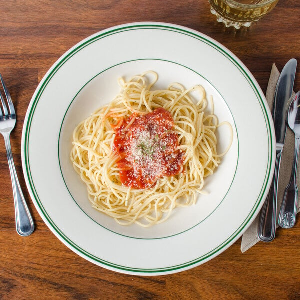 A close up of a Homer Laughlin green banded pasta bowl filled with spaghetti and sauce with parmesan cheese on a table.