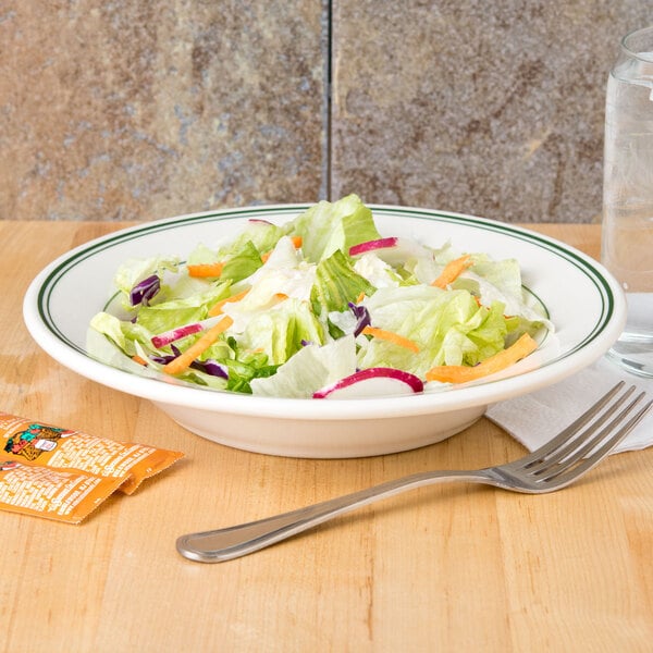 A bowl of salad with lettuce and carrots in a Homer Laughlin green banded soup bowl on a table with a fork and a glass of water.