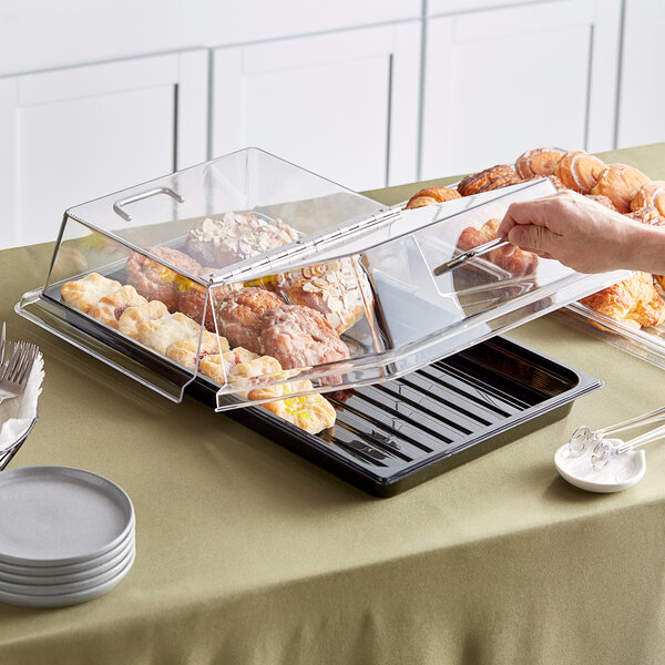 A hand holding a Cambro black polycarbonate tray of pastries on a table.