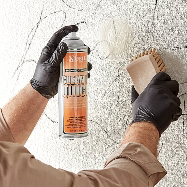 A person in black gloves using Noble Chemical Clean-It-Quick Vandalism Mark Remover to spray a wall.