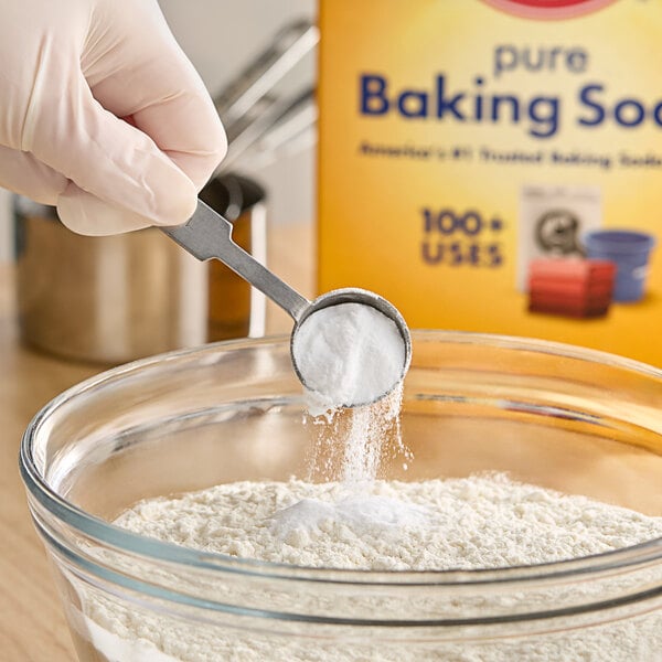 A gloved hand uses a measuring spoon to add Arm & Hammer Baking Soda to a bowl.