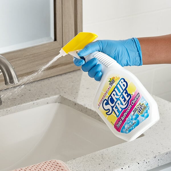 A hand in a blue glove spraying Scrub Free Restroom Cleaner from a white bottle.