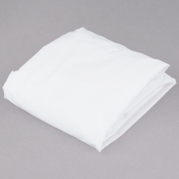 A folded white L.A.Baby fitted crib sheet on a gray surface.