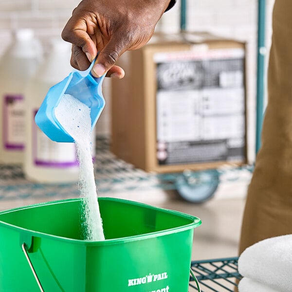 A hand pouring OxiClean Versatile white powder into a green bucket.