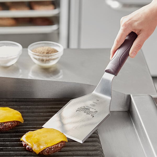 A person using a Mercer Culinary Hell's Handle turner to cook burgers on a grill.