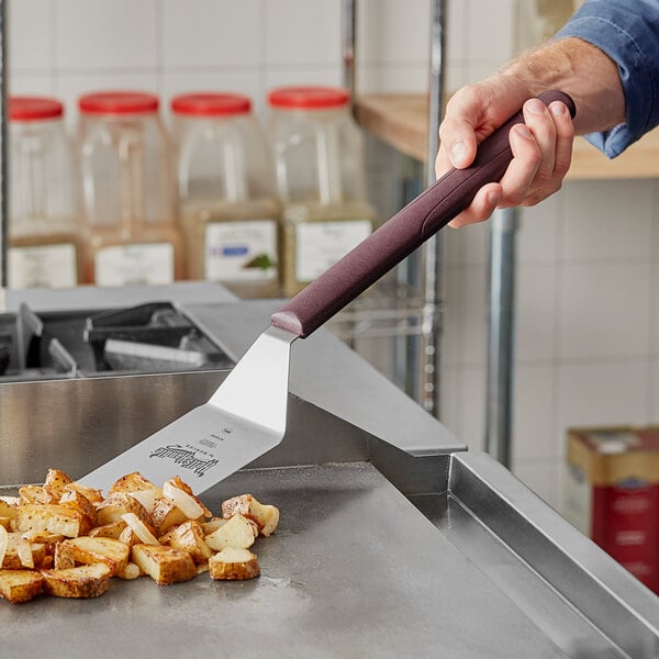 A person using a Mercer Culinary Hell's Handle turner to cut potatoes on a stove.