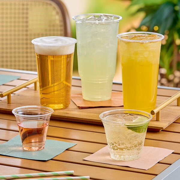A group of clear plastic cups on a table with drinks and straws.