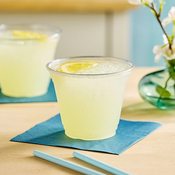 A clear plastic Choice PET cup of lemonade with a blue straw and a lemon slice.