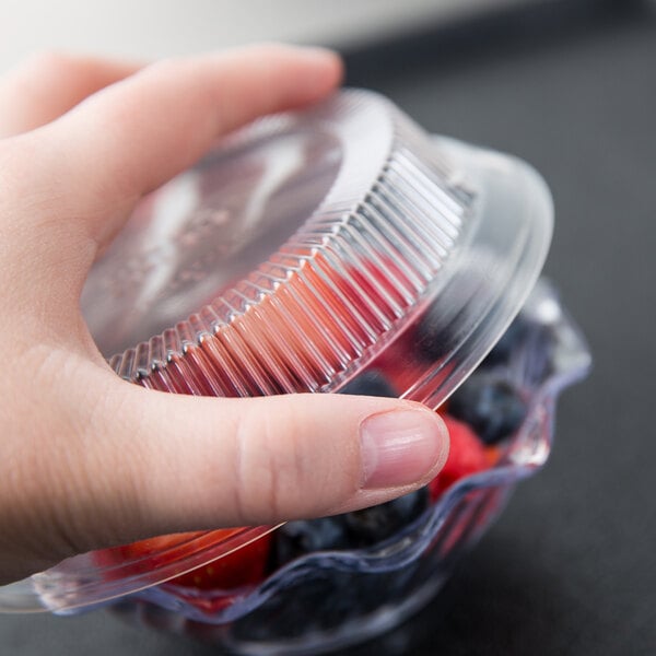 A hand holding a plastic container with blueberries over a counter with dessert dishes.