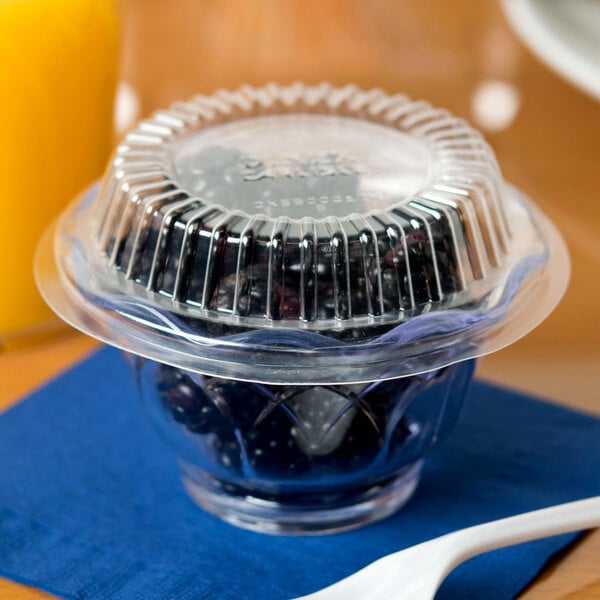 A clear plastic Dinex cup filled with blueberries on a table with a spoon.